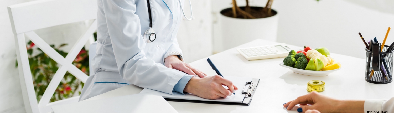 „Ärztin im Gespräch mit Patientin, auf einem Tisch liegen frisches Obst und Gemüse, ein Maßband und ein Klemmbrett – Symbol für ganzheitliche Gesundheitsberatung.“